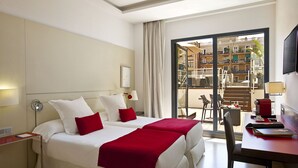 Habitación de hotel con una cama grande, un escritorio y vistas a un balcón con mobiliario exterior.