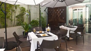 Un área de comedor al aire libre con mesas, sillas, sombrillas y plantas en macetas.