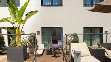 Een moderne buiten zithoek met een grote plantenbak, comfortabele stoelen, een tafel met glazen blad en een grote parasol.