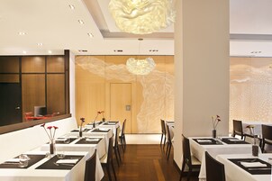 Un ristorante con lunghi tavoli, tovaglie bianche e sottopiatti neri.