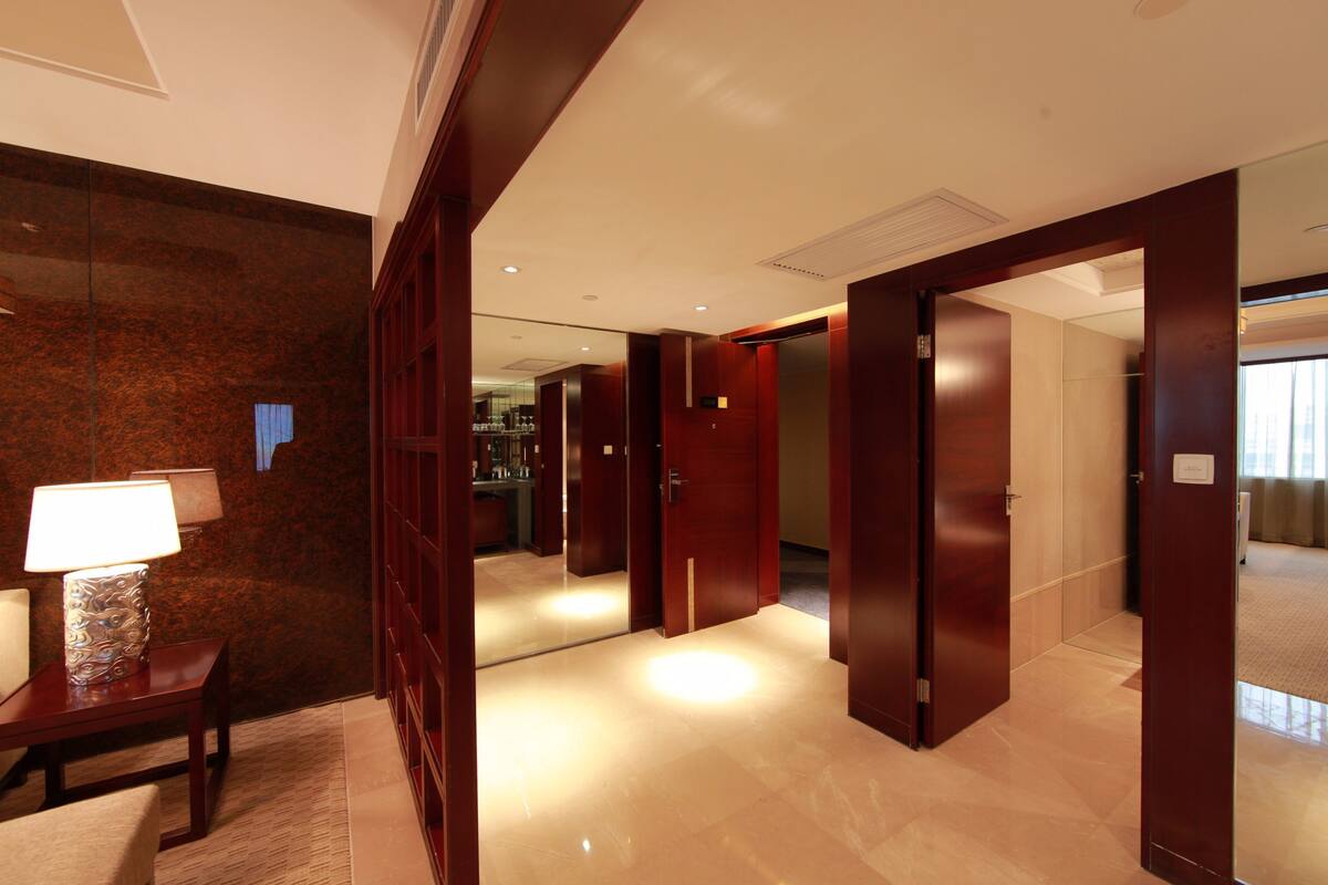 A hotel corridor with wooden doors, a lamp, and a mirror.
