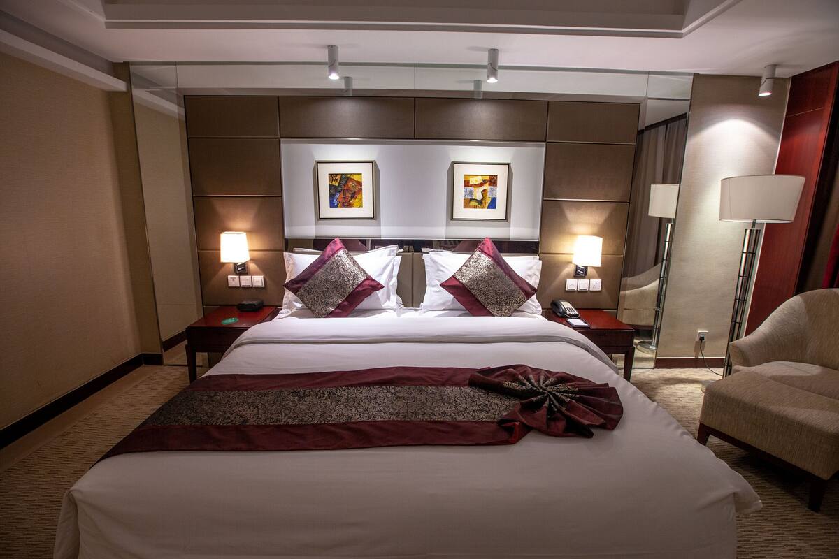 A hotel room with a large bed, two bedside tables, a desk, a chair, and artwork on the wall.