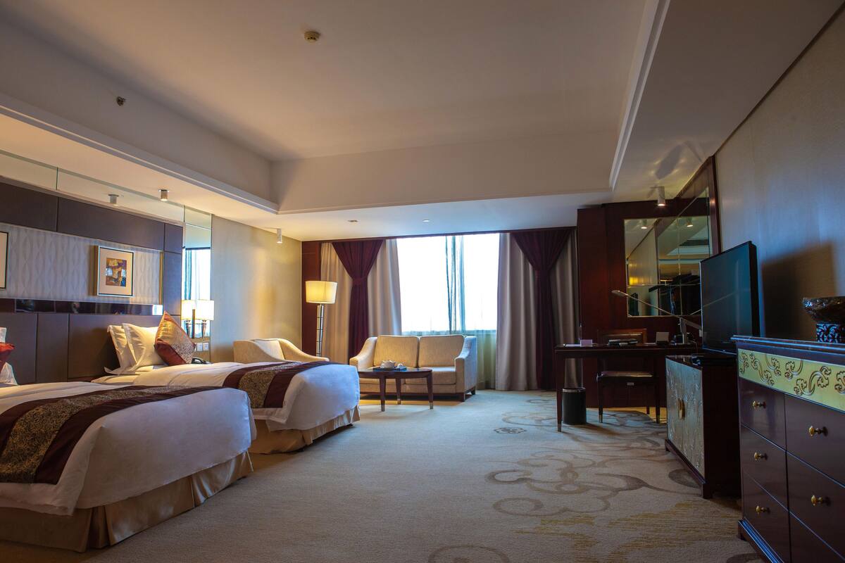 A hotel room with two beds, a desk, a chair, a television, and a dresser.