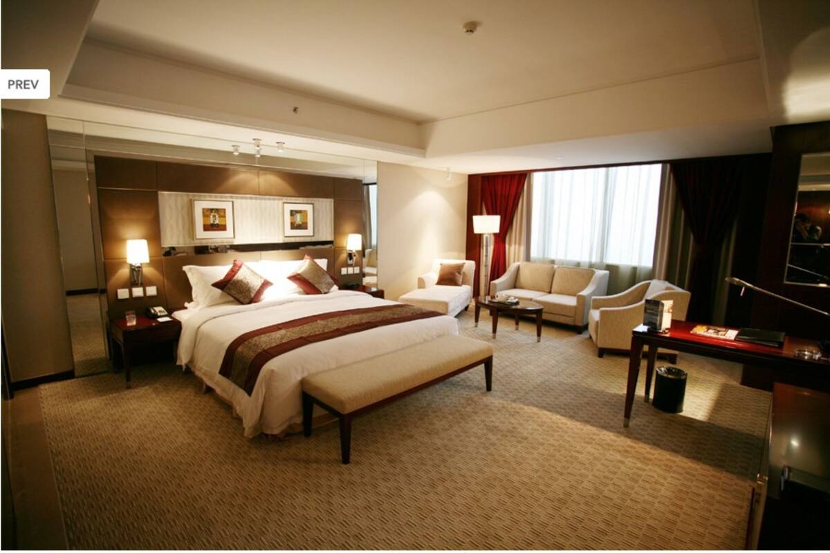 A spacious hotel room with a large bed, a sofa, a desk, and a TV.