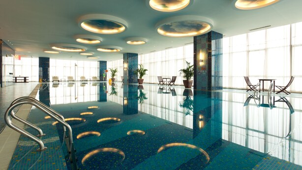 Una piscina interna con vista chiara sul soffitto, ampie finestre e una zona relax con tavoli e sedie.