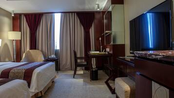 A hotel room with two beds, a desk, a chair, a TV, and a large window with curtains.
