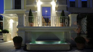 A grand entrance with a lit-up blue door, a fountain, and a balcony with a railing. - Hotel Villa Duse (Rome)