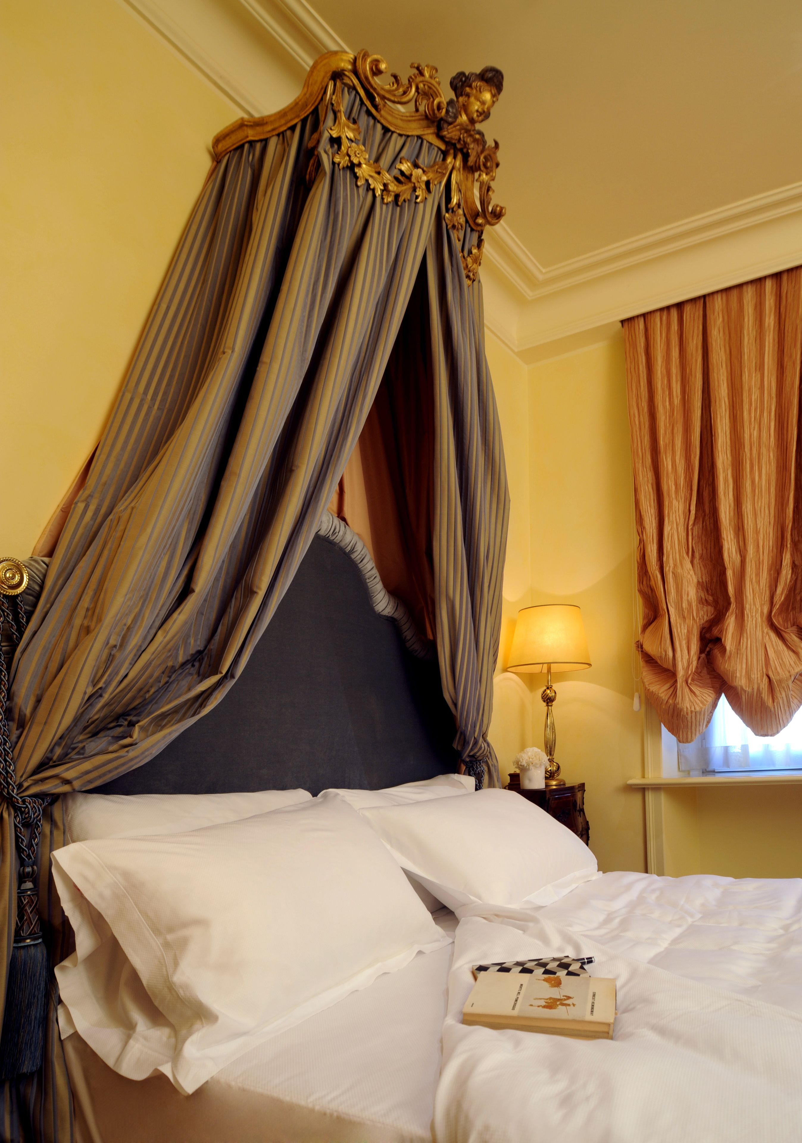 A bed with a canopy, white linens, and a book on it.