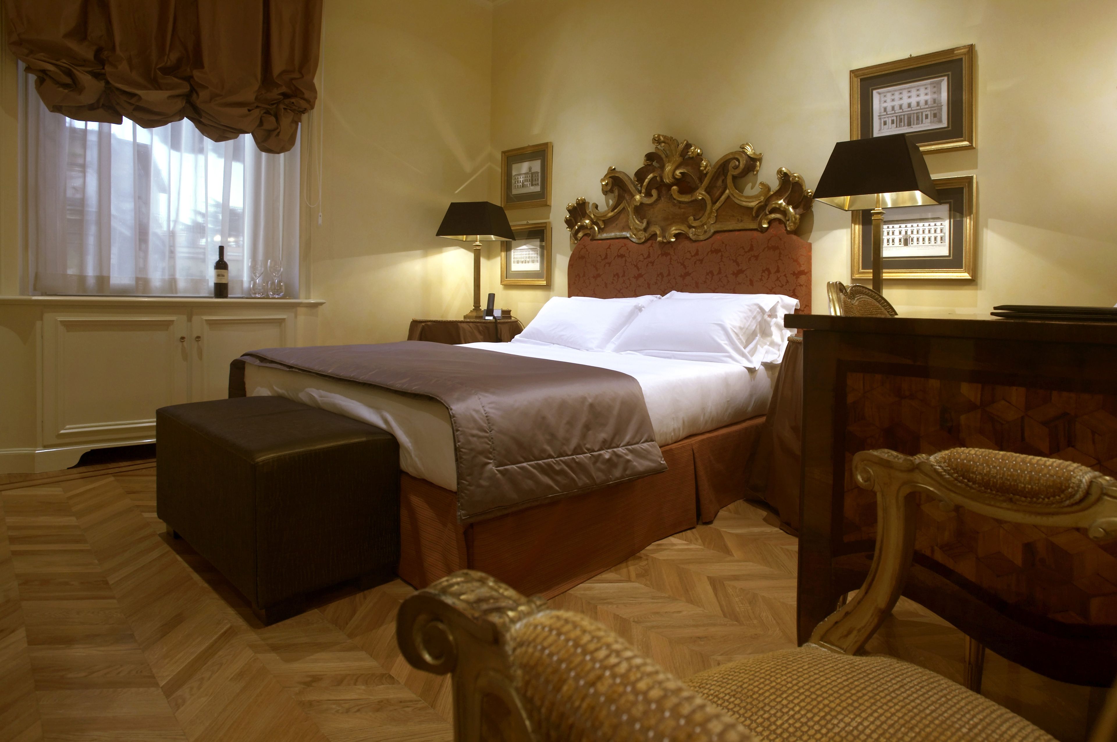 Ein Hotelzimmer mit einem großen Bett, Holzboden, einem Nachttisch mit Lampe, einem Sessel und einem Fenster mit Vorhängen.