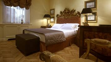 Ein Hotelzimmer mit einem großen Bett, Holzboden, einem Nachttisch mit Lampe, einem Sessel und einem Fenster mit Vorhängen.