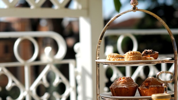 A three-tiered tea service stand with pastries, a teapot, cups, and a rose on a table. - Hotel Villa Duse (Rome)