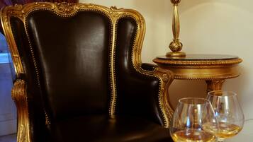 A black leather chair with gold trim, a gold-framed mirror, and a table with a gold lamp and wine glasses.