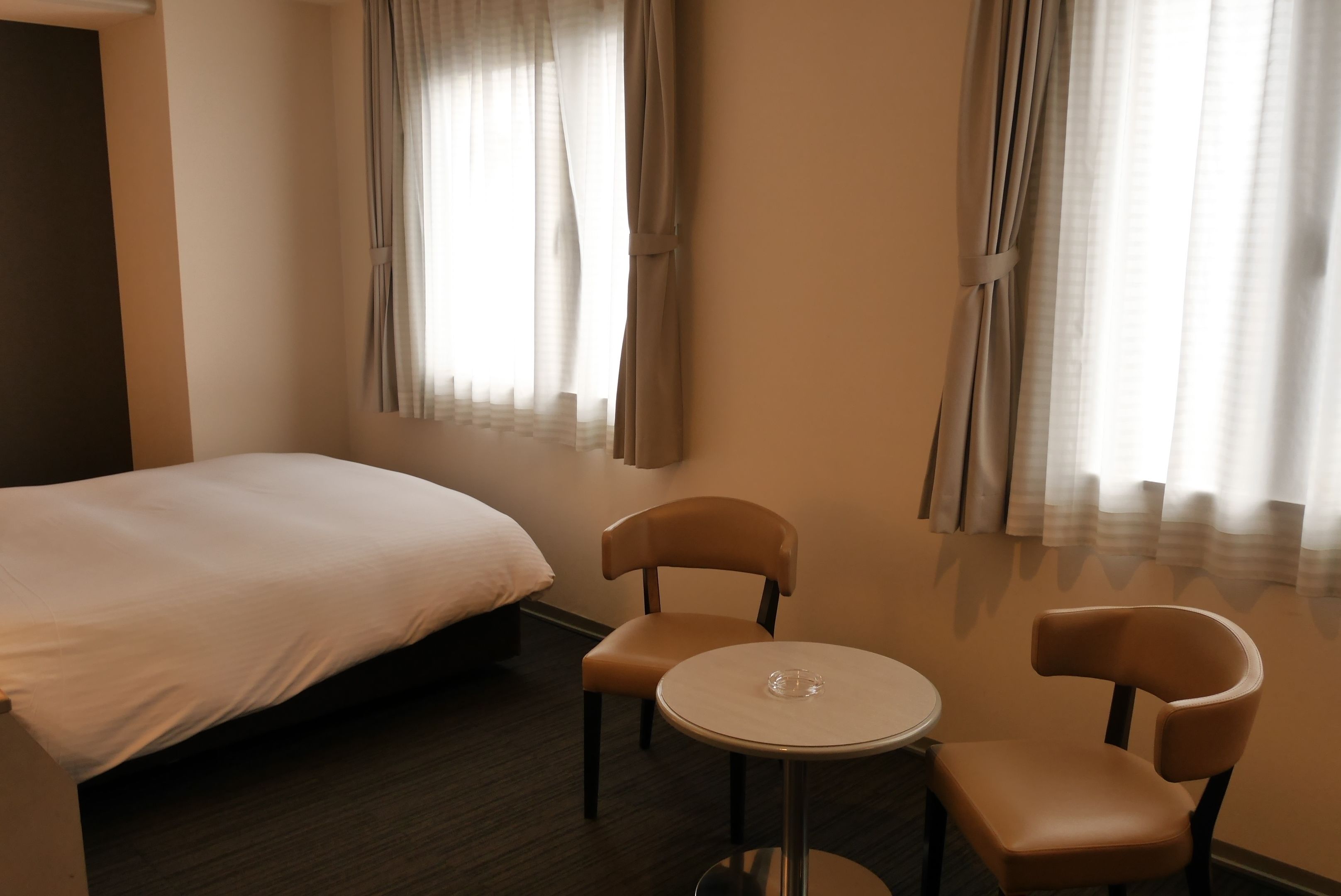 A hotel room with a bed, two chairs, a small round table, and curtains on the windows.
