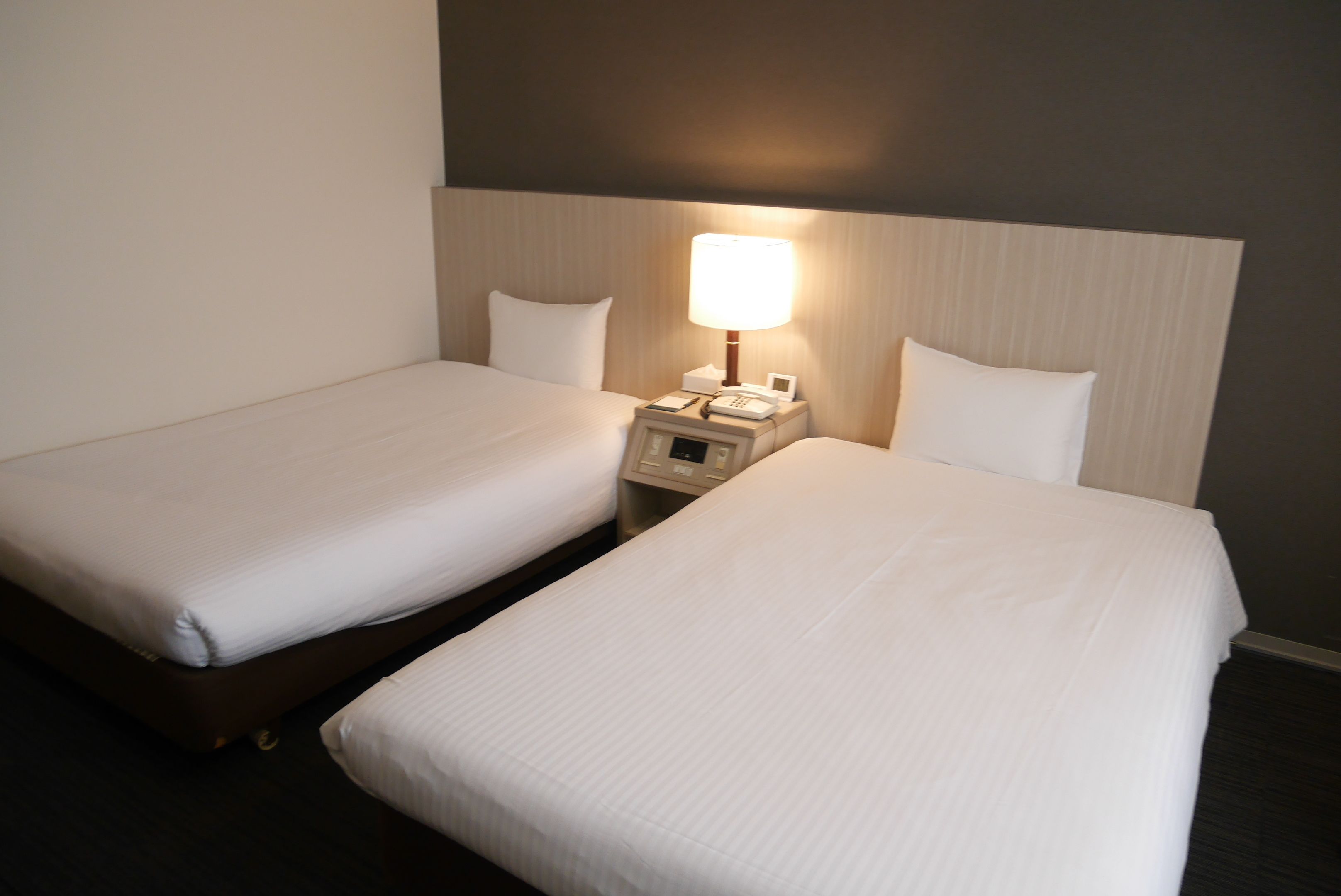Ein Hotelzimmer mit zwei Einzelbetten, einem Nachttisch mit Lampe und einem Telefon.