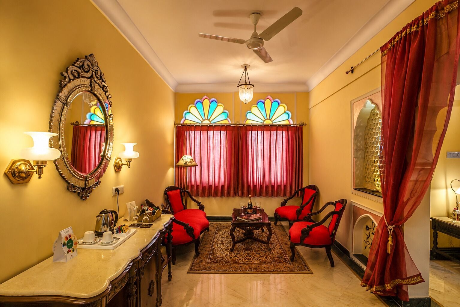A room with a chandelier, a ceiling fan, a large mirror, red curtains, and a red sofa set.