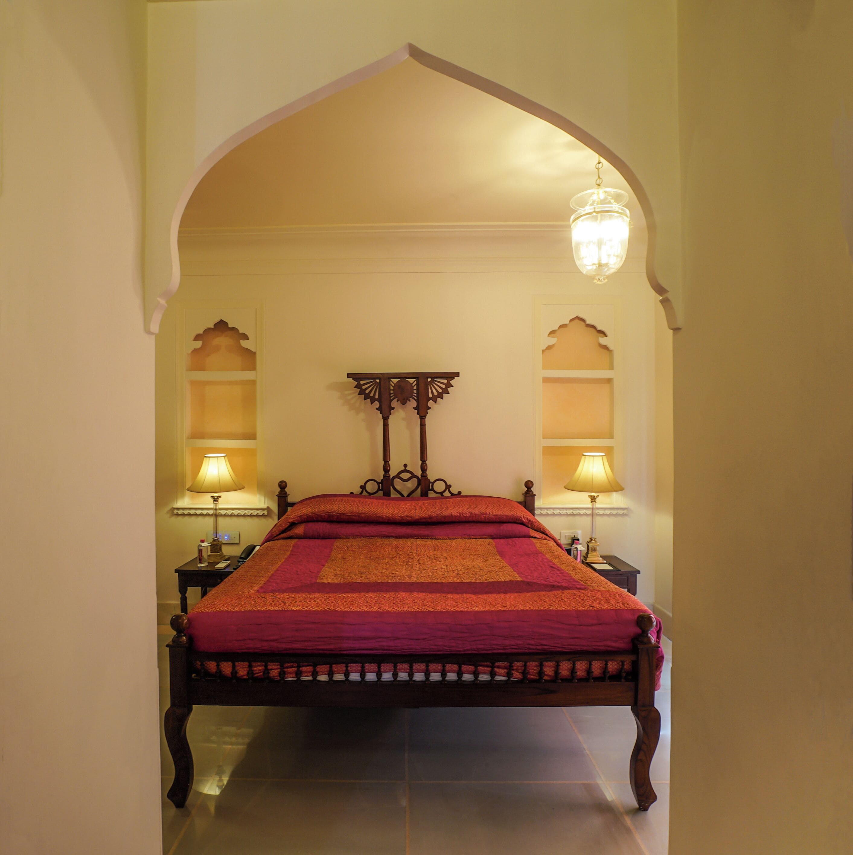 A bed with a headboard, two bedside tables, lamps, and an arched doorway.