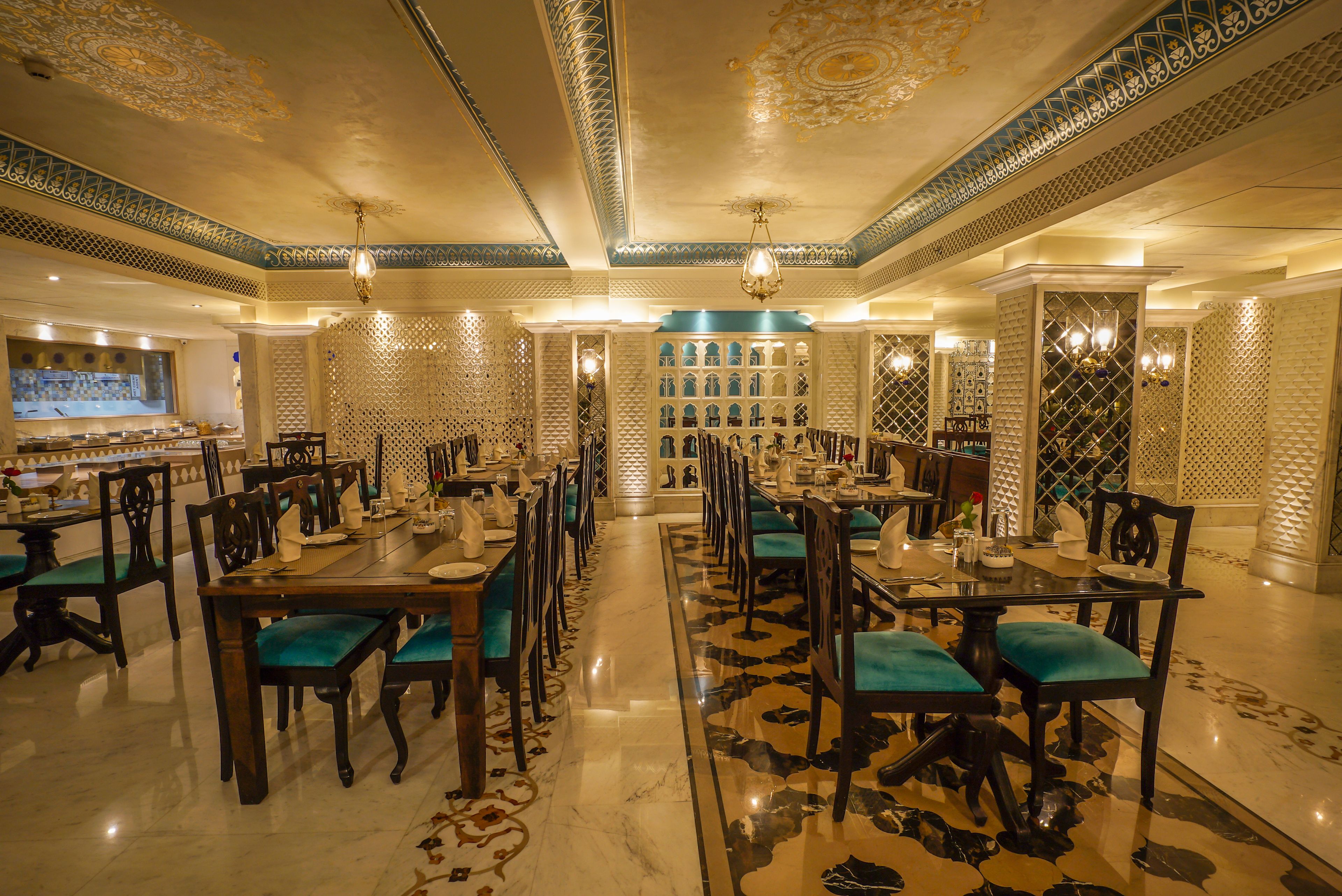 Un vaste espace dédié à la salle à manger, avec de nombreuses tables et chaises, des motifs décoratifs au plafond et un sol à motifs.