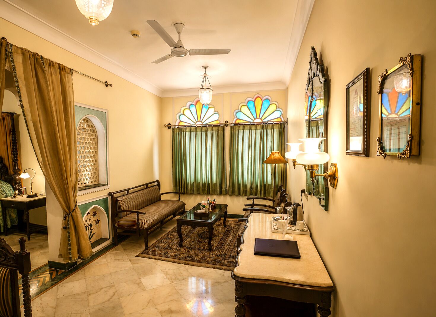 A room with a ceiling fan, a sofa, a coffee table, a side table with a lamp, and a mirror on the wall.