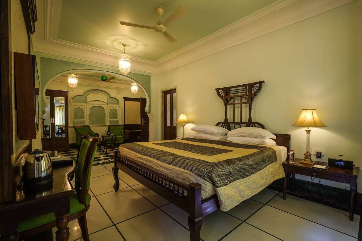 Een hotelkamer met een bed, een bureau, een stoel, een nachtkastje, een lamp, een klok en een plafondventilator.