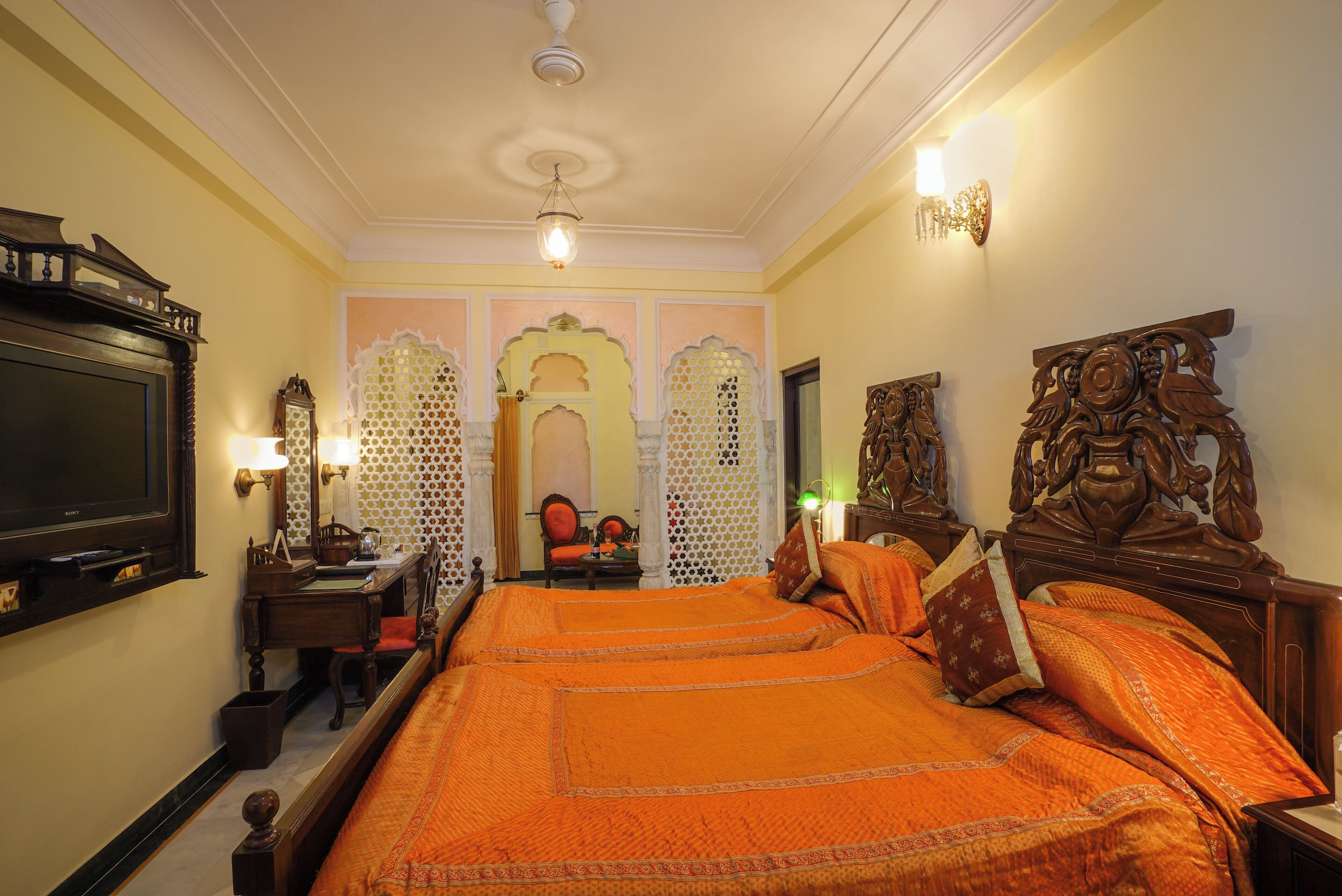 A hotel room with a large bed, a television, a desk with a computer, and a decorative wall.