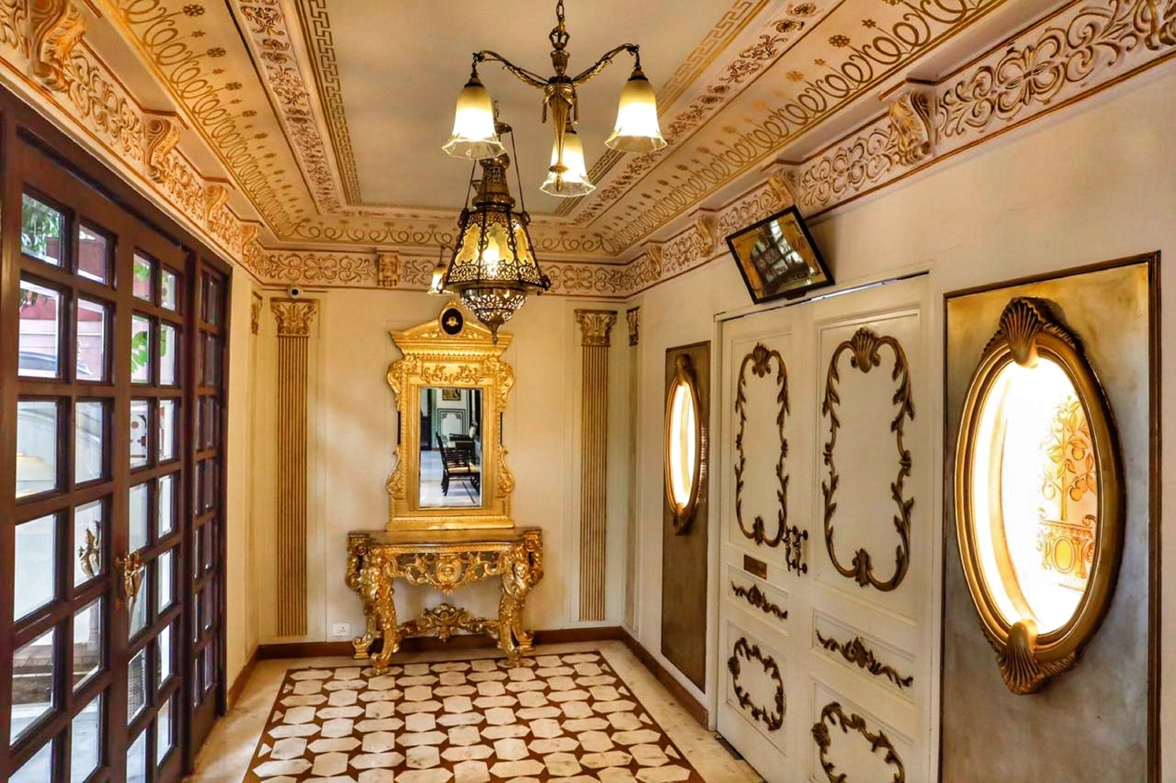 Um corredor ricamente decorado com um espelho ornamental, um candelabro e piso estampado.