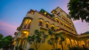 Un hotel de varios pisos con balcones, ventanas arqueadas y un patio con palmeras.