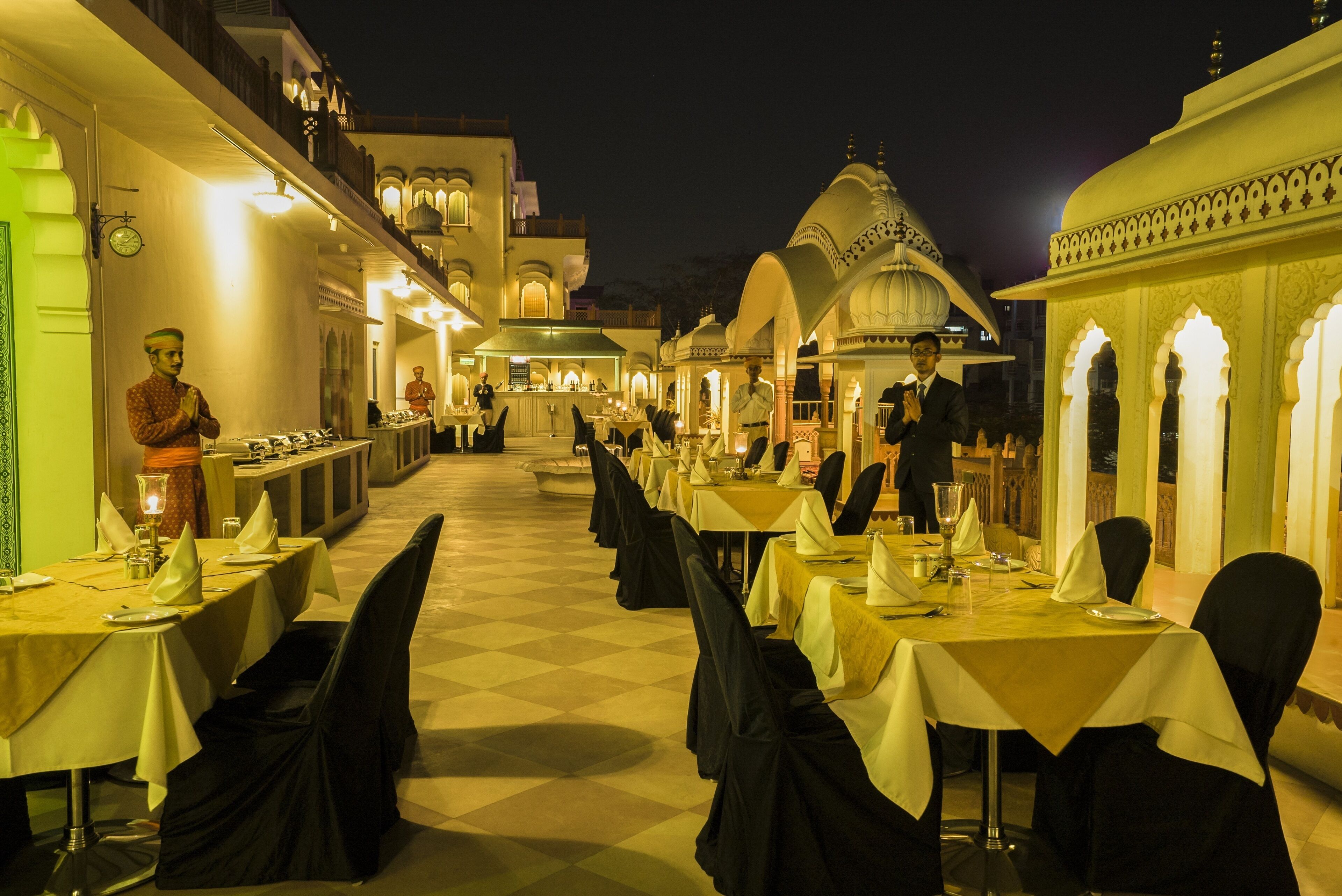 A well-lit dining area with tables set for guests, featuring a checkered floor and traditional architectural elements.