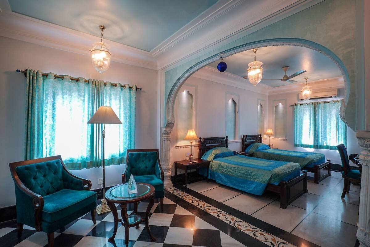 Een hotelkamer met twee bedden, een zithoek met een stoel en een tafel, een kroonluchter en een plafondventilator.