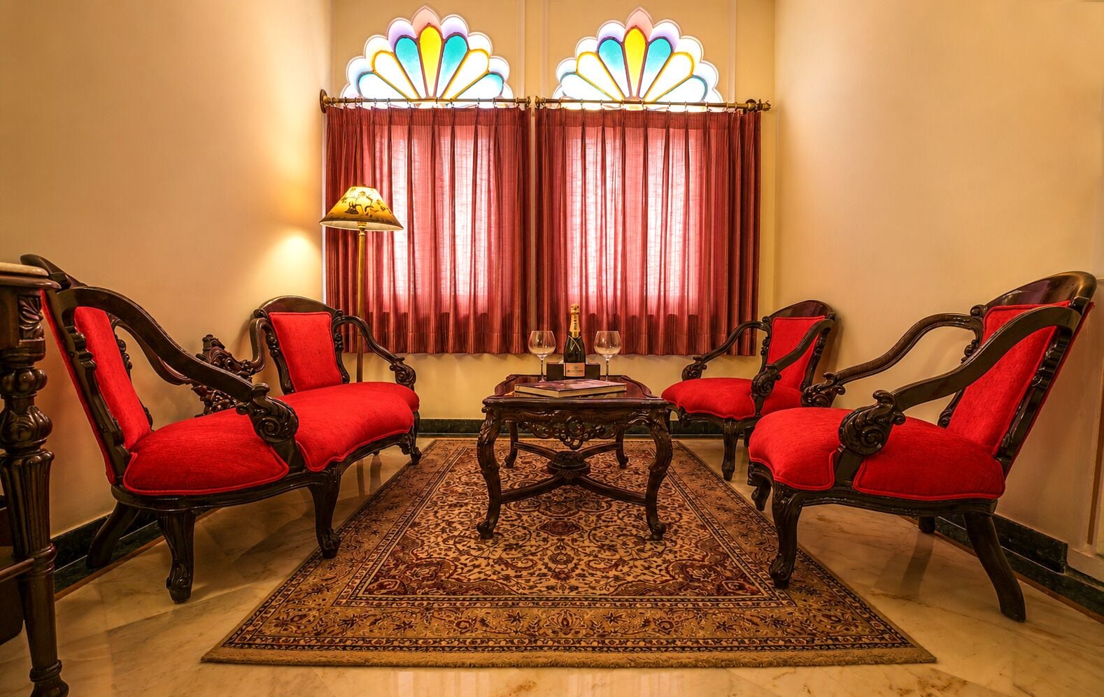 Une pièce comprenant quatre chaises en bois richement décorées, dotées de coussins rouges, un tapis à motifs et une table sur laquelle se trouvent une bouteille et un verre.