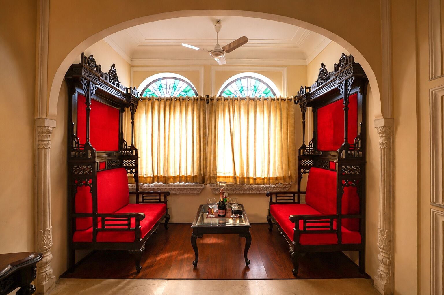 Una habitación con dos sillones tapizados en rojo, una mesa de centro de madera y un ventilador de techo.