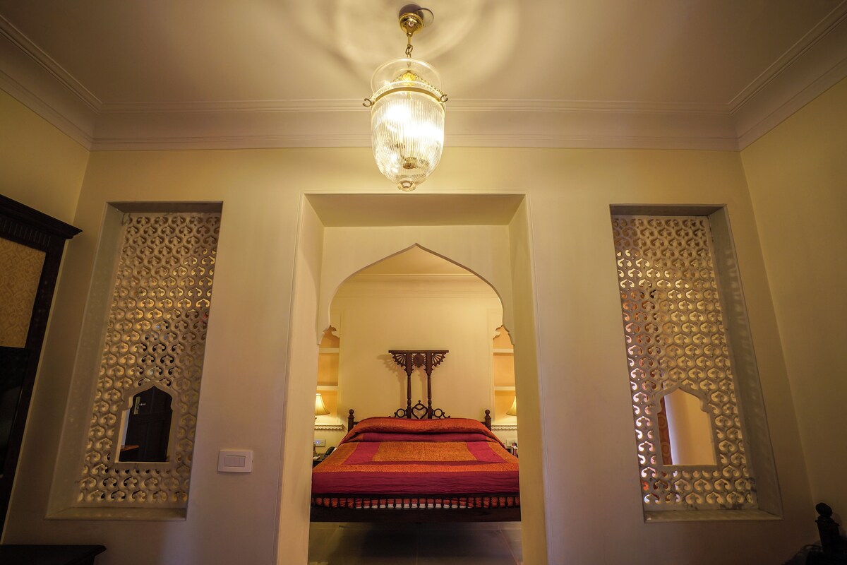 Ein rundbogiger Durchgang zu einem Raum mit einem Bett, einer Chandelier und dekorativen Wandverkleidungen.