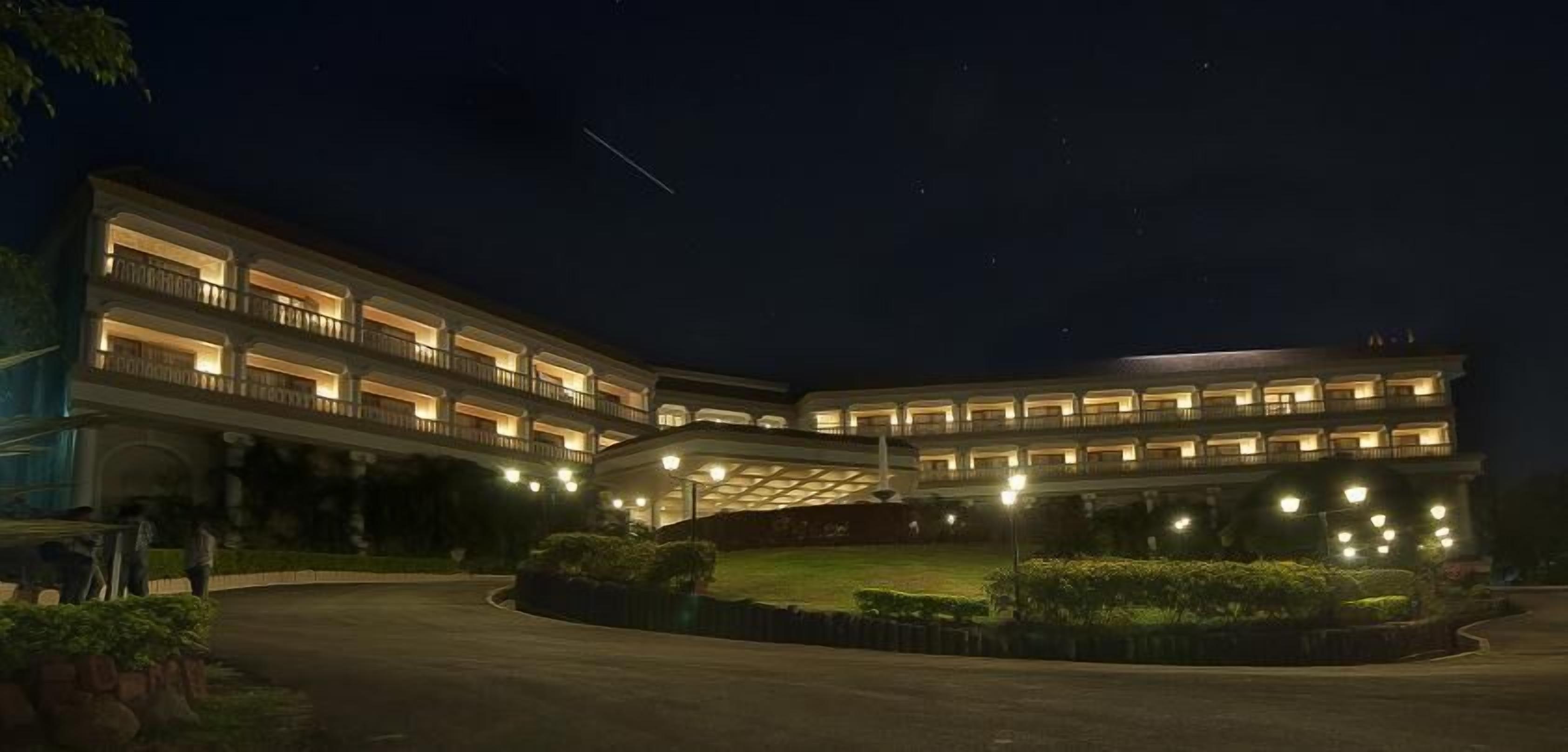 Un hotel de varios pisos con fachada curva, balcones iluminados y un césped bien cuidado.