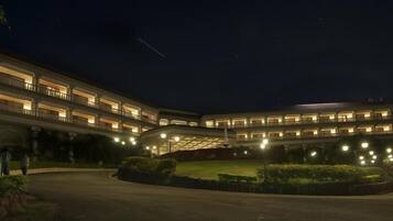 Un hotel de varios pisos con fachada curva, balcones iluminados y un césped bien cuidado.