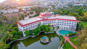 A large, multi-story building with a red roof and white exterior, surrounded by lush greenery and a central pond. - Lagoona Resort (Mawal)
