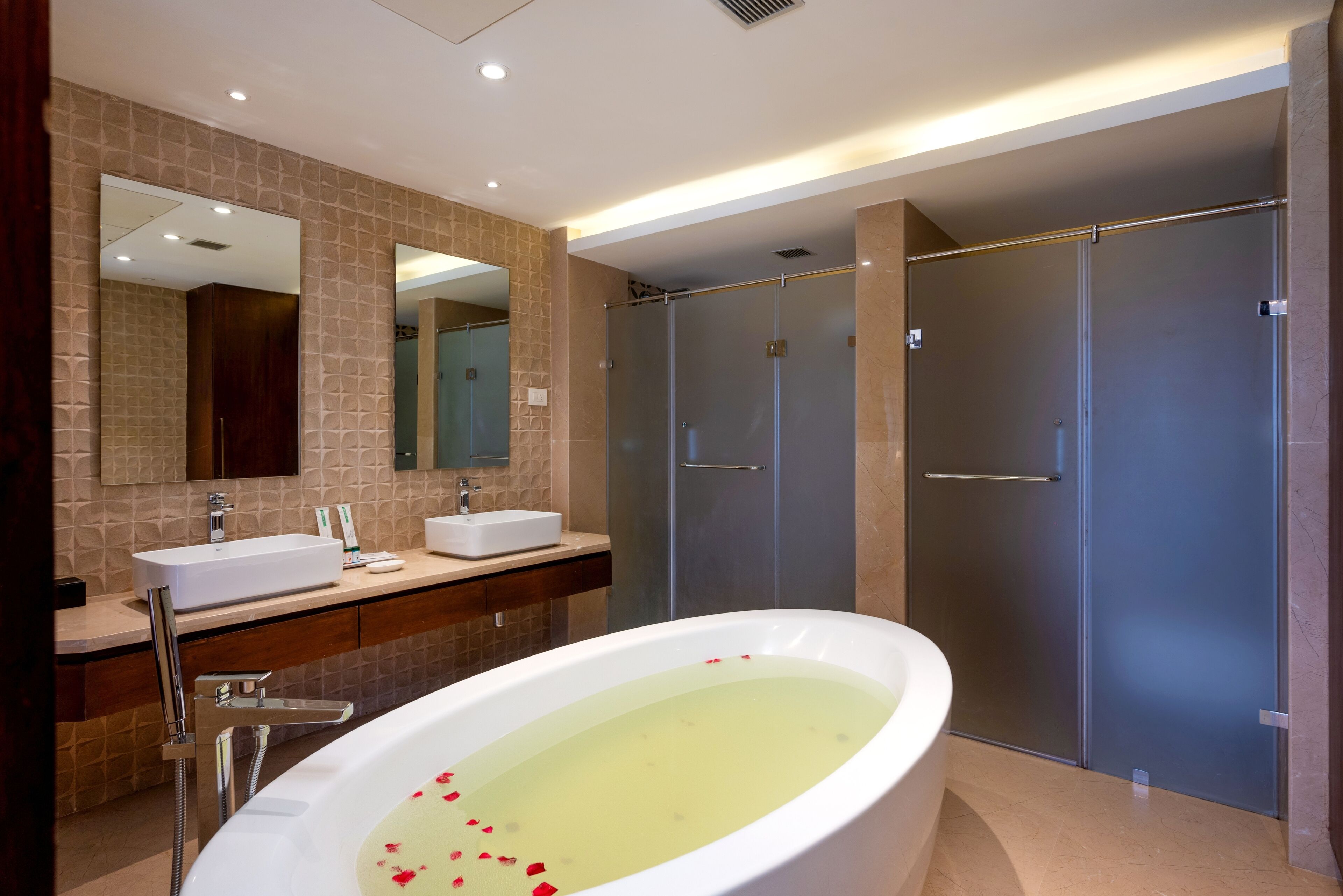A modern bathroom with a large bathtub, two sinks, a mirror, and a walk-in shower.