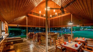 An indoor dining area with wooden tables and chairs, a bar, and a view of the outdoors. - Lagoona Resort (Mawal)
