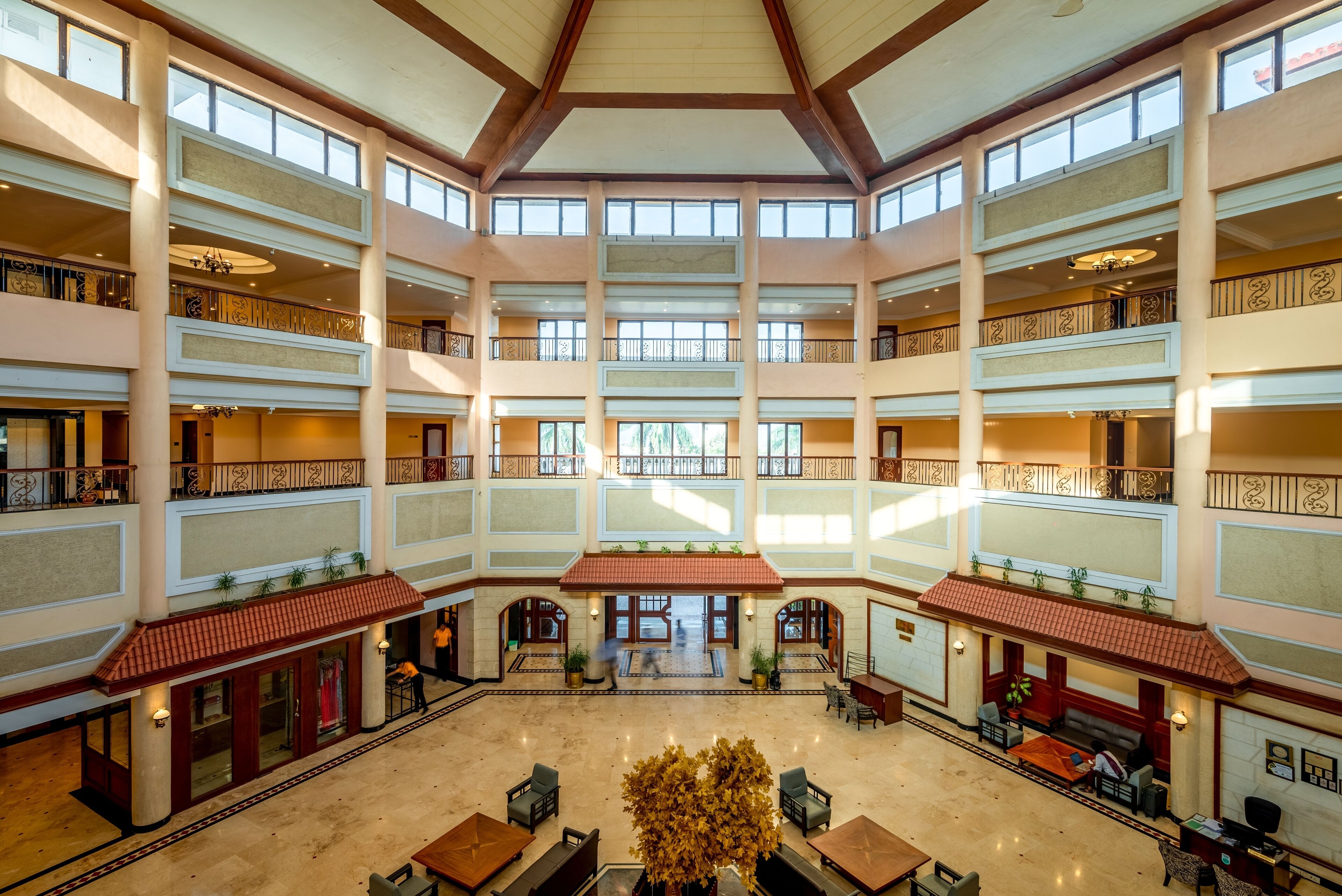 A multi-level atrium with a central open space, balconies on each floor, and a large tree in the center.
