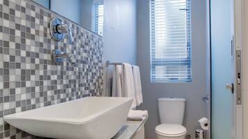 A modern bathroom with a large vessel sink, a toilet, and a window with blinds.