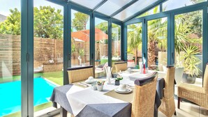 Un hivernacle amb vista a la piscina, mobles de vimet i una taula preparada per dinar.