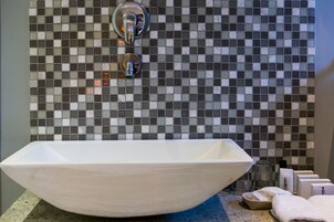 A bathroom with a white vessel sink, a tiled backsplash, and toiletries on the counter.