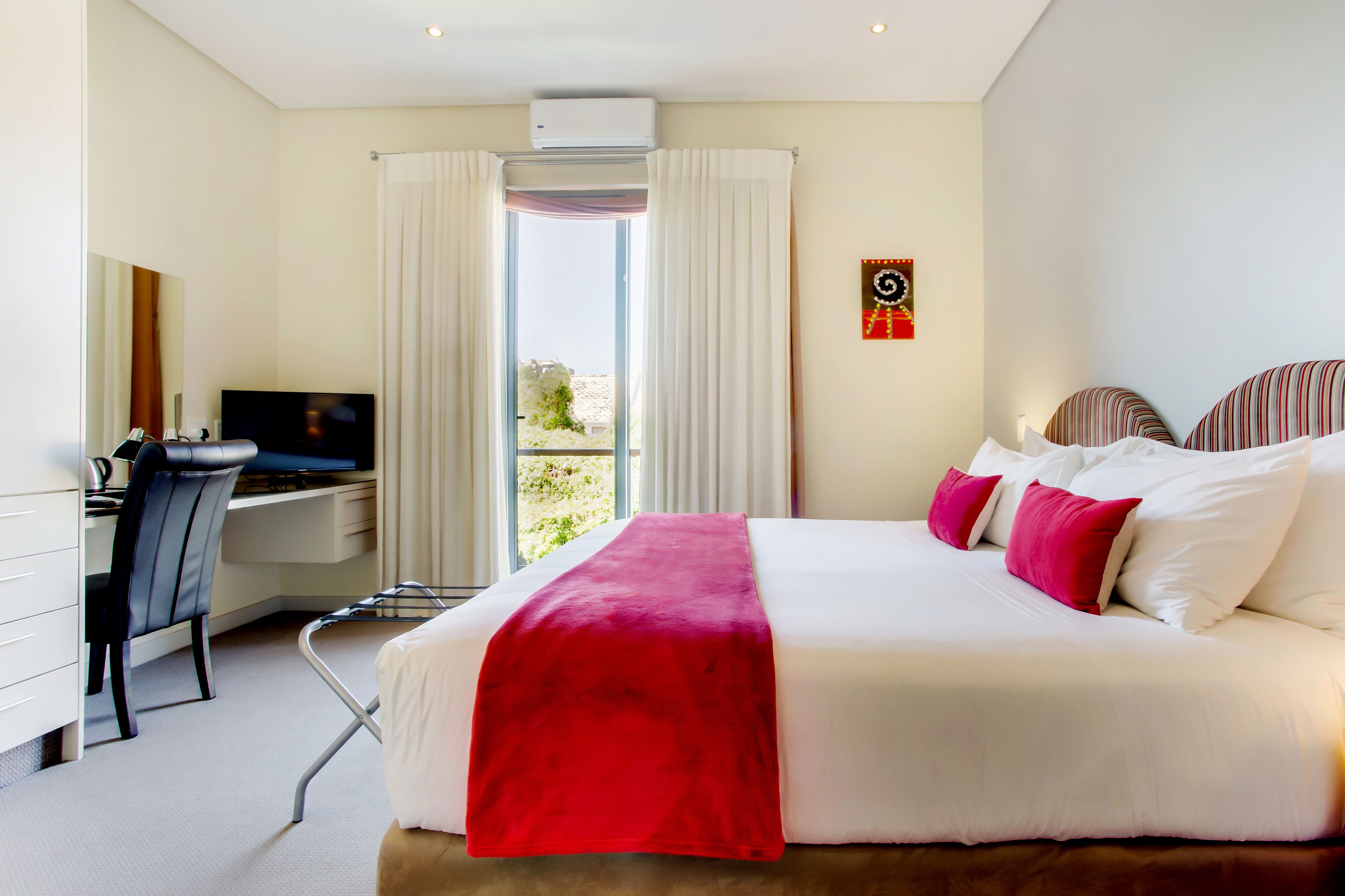 A hotel room with a bed, a desk, a chair, a television, and a window with curtains.