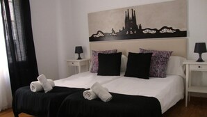 A double bed with black and white bedding, two nightstands with lamps, and a cityscape painting above the bed. - Petit Hotel (Barcelona)