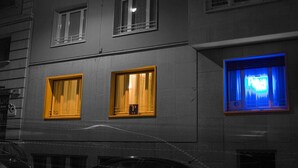 A building with three windows, one with a yellow frame and another with a blue frame, and a visible 'P' sign on the wall. - Petit Hotel (Barcelona)