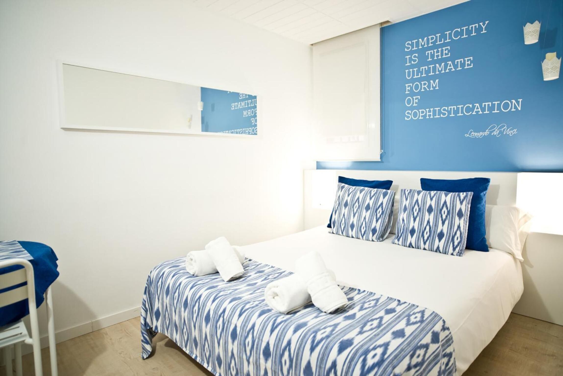 Une chambre d’hôtel avec un lit, une chaise et un mur orné d’une citation.