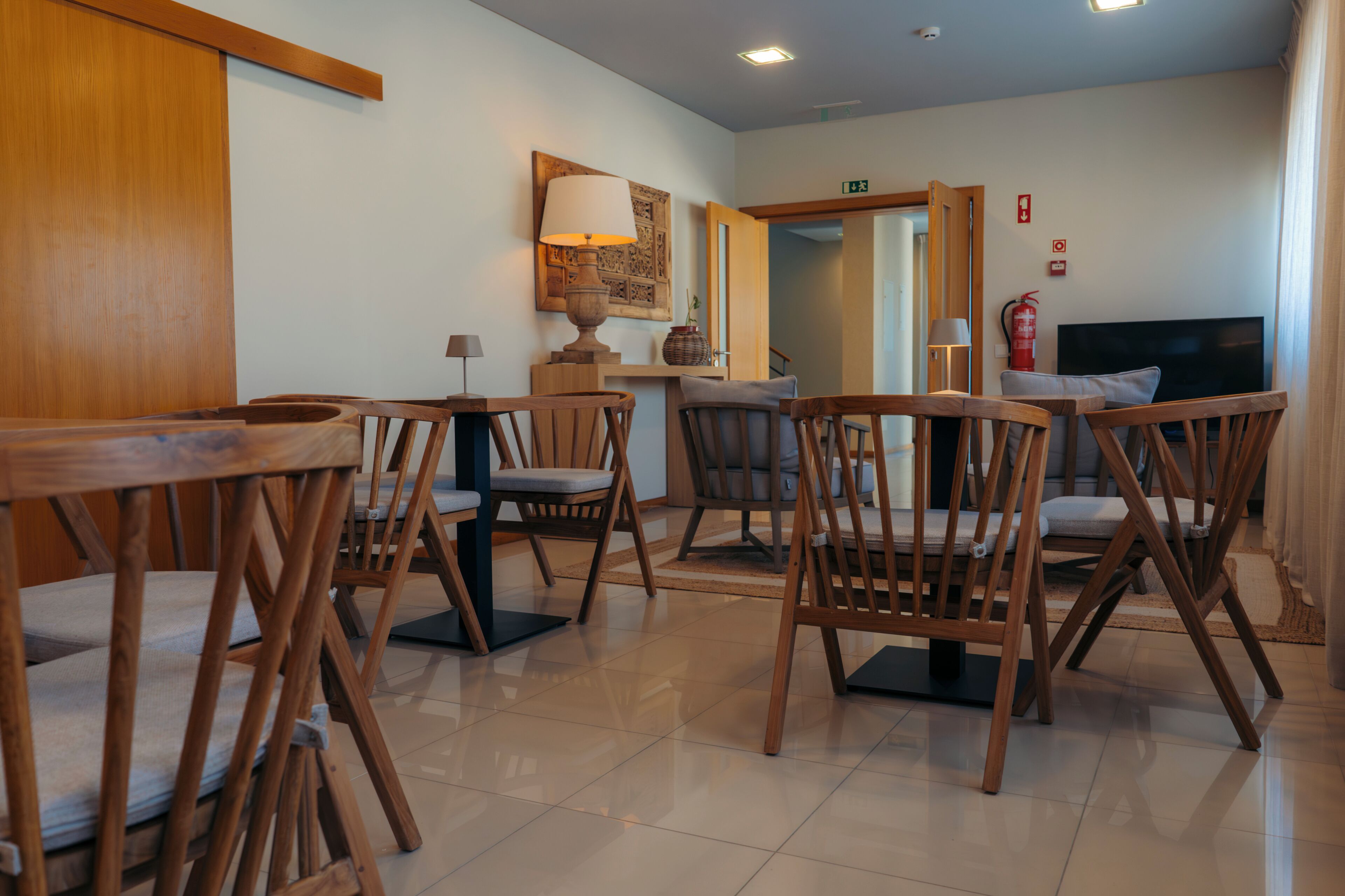 Een eetgedeelte met houten stoelen en tafels, een lamp, een brandblusser en een televisie.