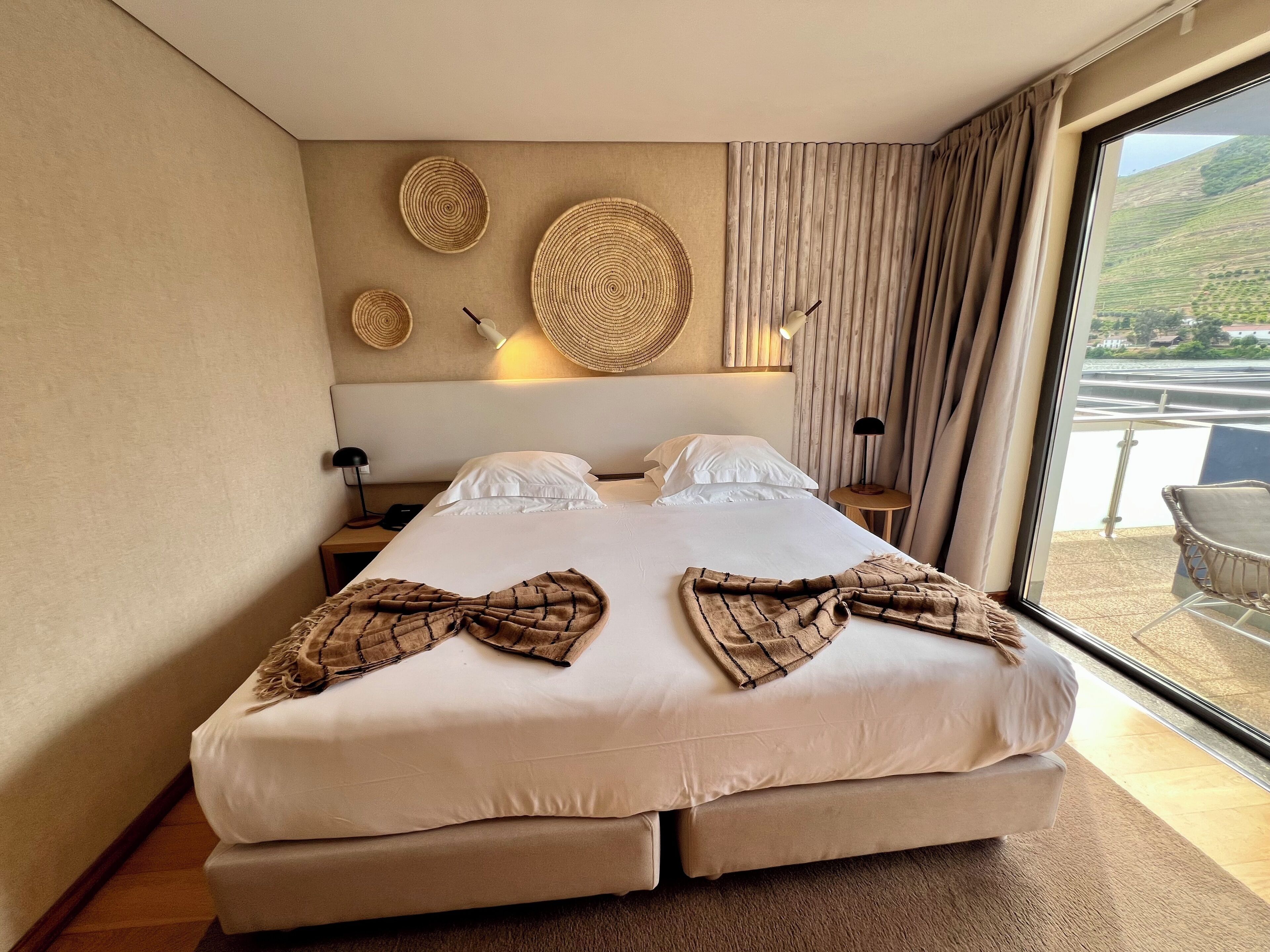 A large bed with a headboard, two bedside tables, and a view of a balcony with outdoor seating.