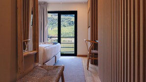 A bedroom with a bed, a bench, and a view of a vineyard through a large window. - Hotel Folgosa Douro (Armamar)
