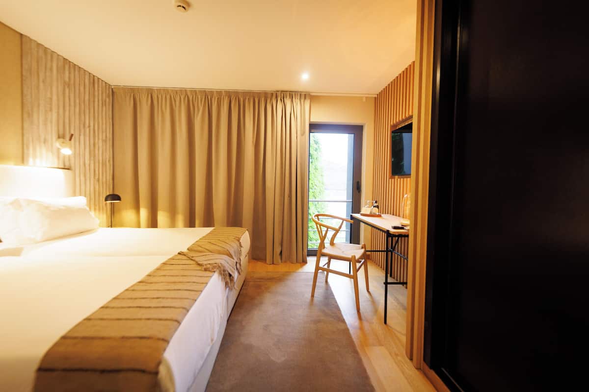 A hotel room with a bed, a desk, a chair, and a large window.