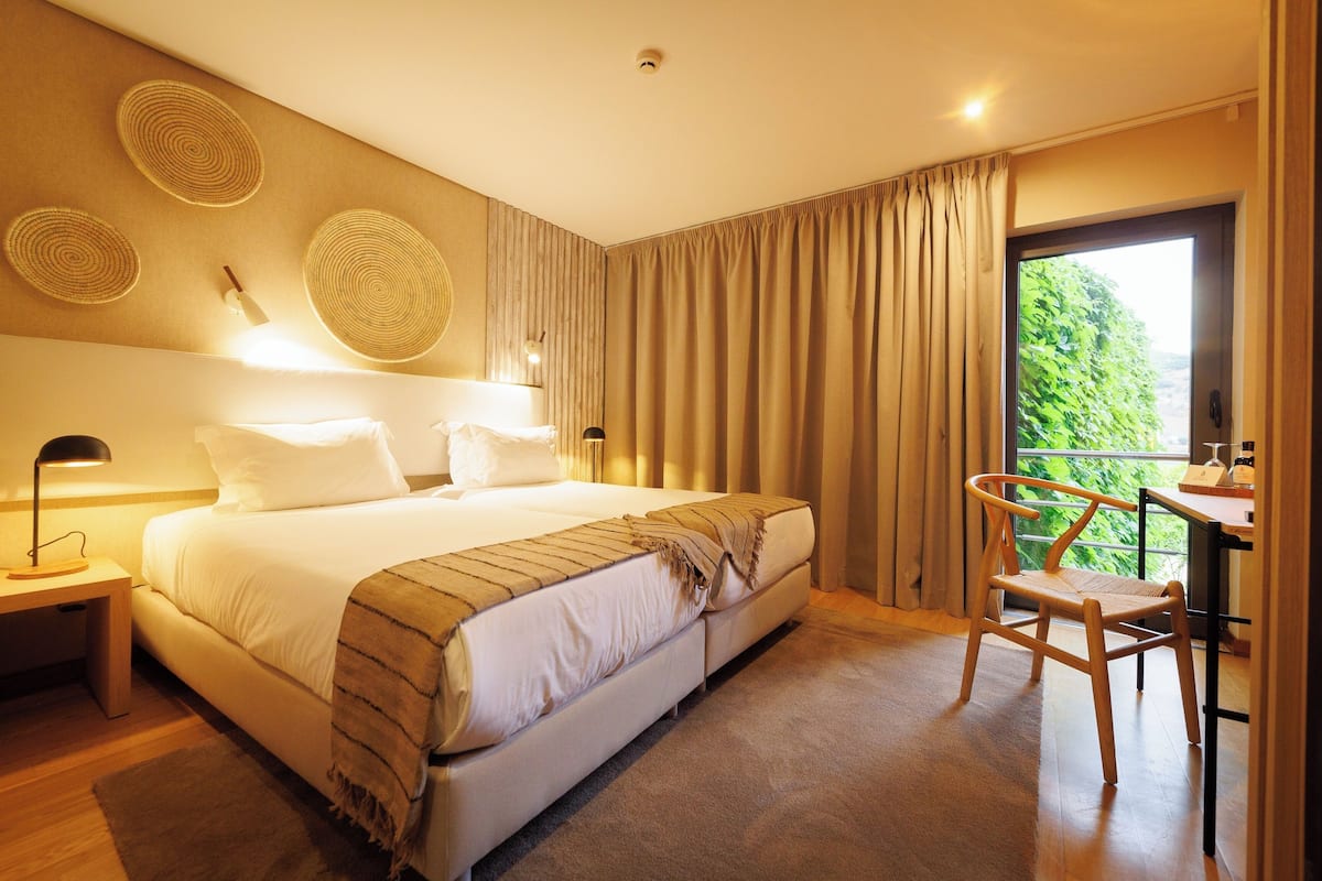 A hotel room with a large bed, a desk with a chair, and a balcony with curtains.