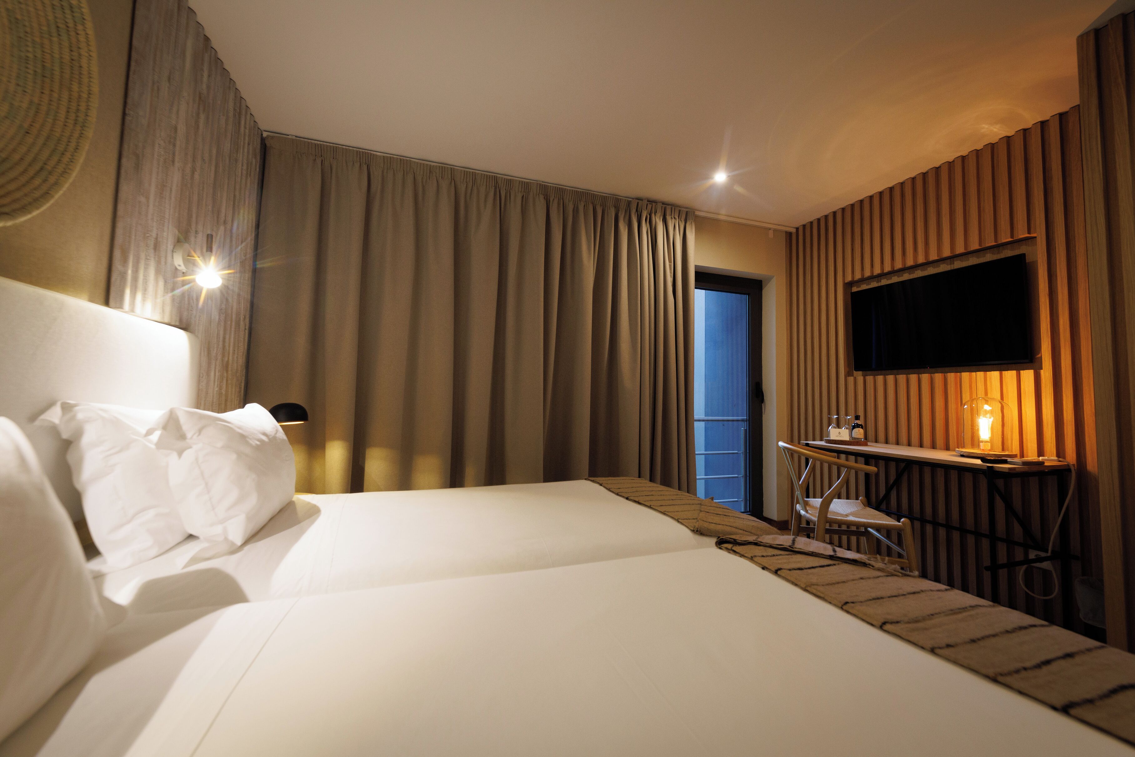 A hotel room with two beds, a desk with a chair, a television, and a window with curtains.